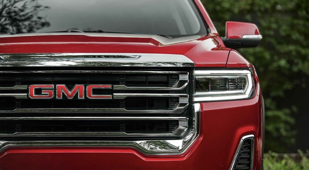 A close up of the grille and headlight on a red 2023 GMC Acadia SLT for sale at a GMC dealer in Mankato.