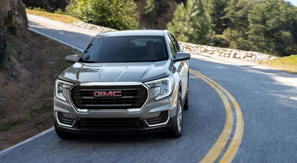 A silver 2022 GMC Terrain is shown from the front driving on a winding road after leaving a used GMC dealer.