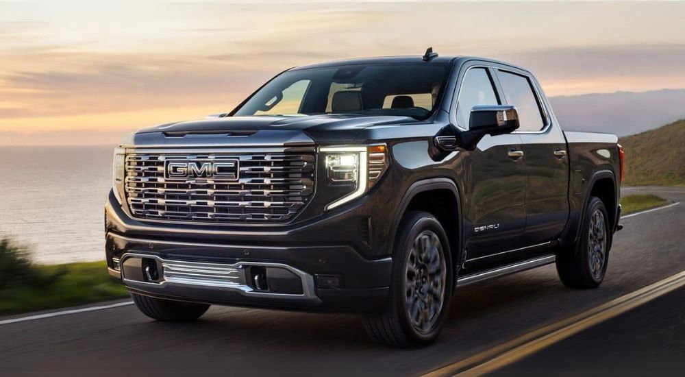 A black 2024 GMC Sierra 1500 for sale is shown driving on a winding road.