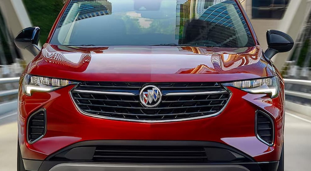 A close up of the front of a red 2024 Buick Envision for sale driving on a bridge.