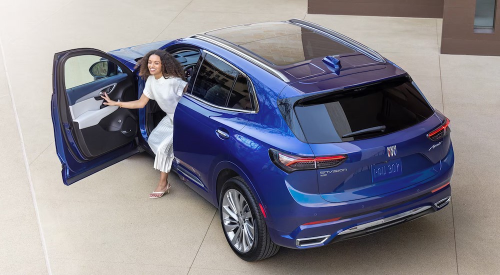 A woman is getting out of the driver's seat of a blue 2024 Buick Envision Avenir near a Mankato car dealer.
