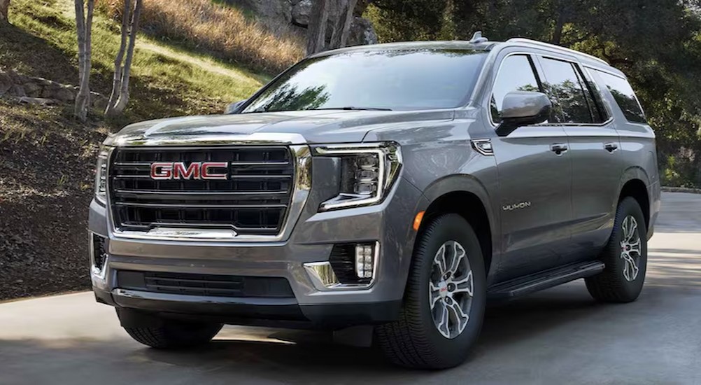 A silver 2024 GMC Yukon XL is driving on a wooded road after visiting a Mankato car dealer.