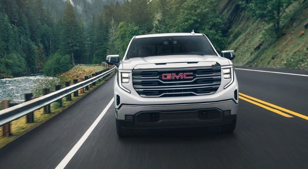 A white 2024 GMC Sierra 1500 for sale near Owatonna is shown driving near a river.