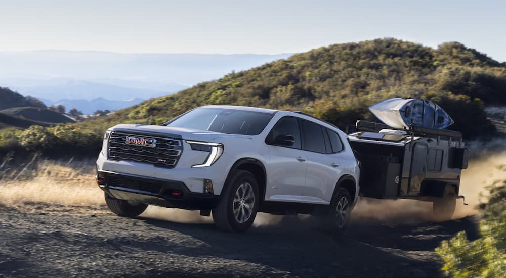A white 2025 GMC Acadia AT4 off-roading with a camper.