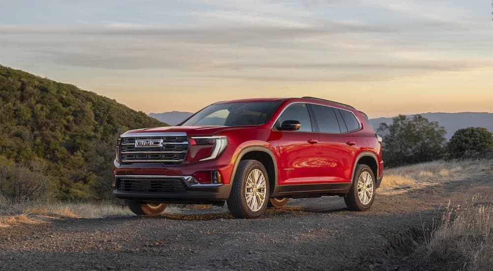 A red 2025 GMC Acadia for sale in Mankato parked on a dirt path.