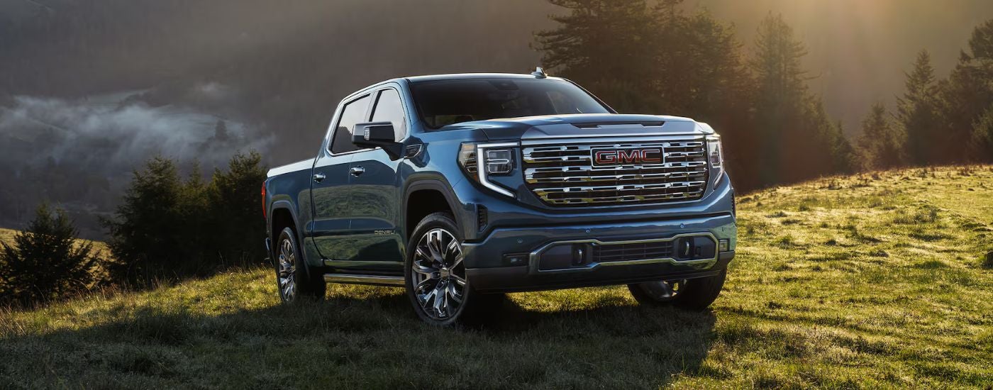 Blue 2026 GMC Sierra 1500 in a green valley at sunrise.