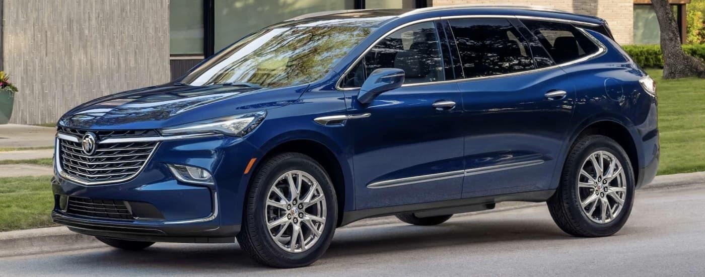 A blue 2023 Buick Enclave is shown parked on the side of a street near a grassy lawn.