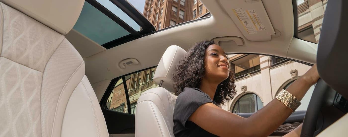 A woman driving through the city in a 2023 Buick Envision with moonroof and white leather interior.