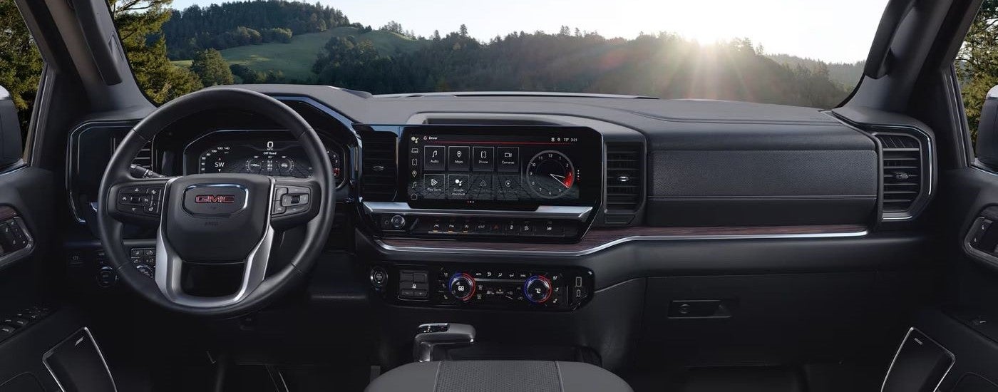The black interior of a 2024 GMC Sierra 1500 shows the steering wheel and infotainment screen.