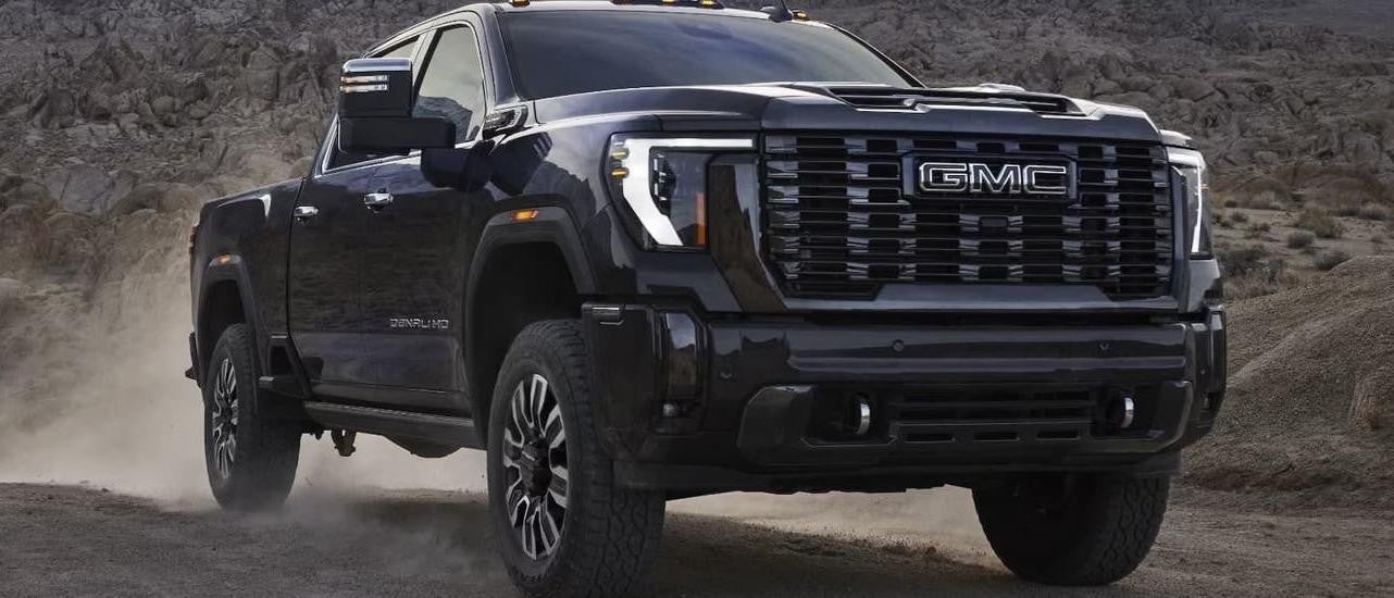 A black 2025 GMC Sierra 2500 HD Denali is driving on a dusty dirt road.