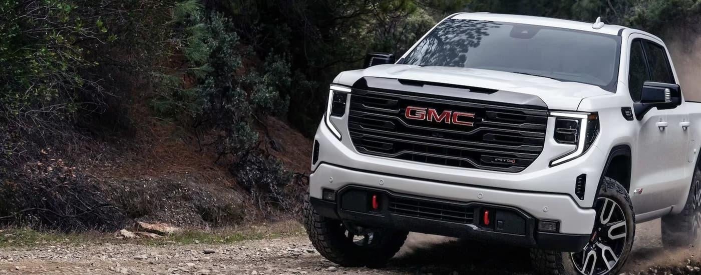 A white 2023 GMC Sierra 1500 AT4 is shown off-roading after leaving a GMC dealer.
