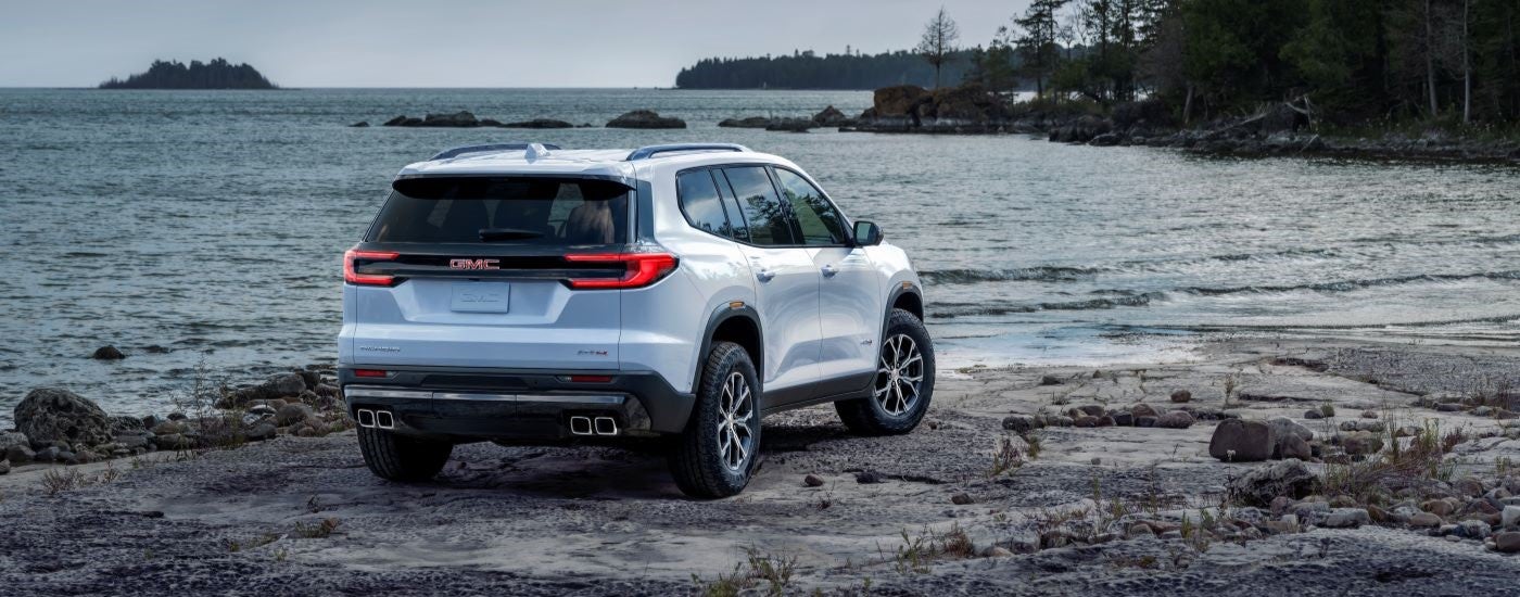 Rear view of a white 2024 GMC Acadia AT4 parked near a shore.