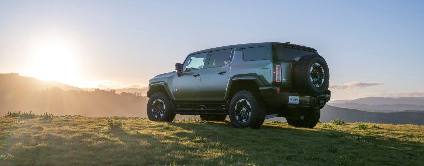 A green 2024 GMC Hummer EV parked on a grassy hill.