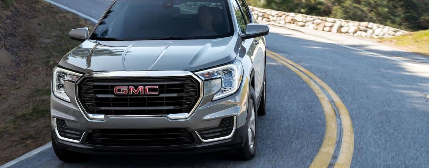 A silver 2022 GMC Terrain SLT is shown from the front driving down a winding hillside road after visiting a GMC dealer in Mankato.