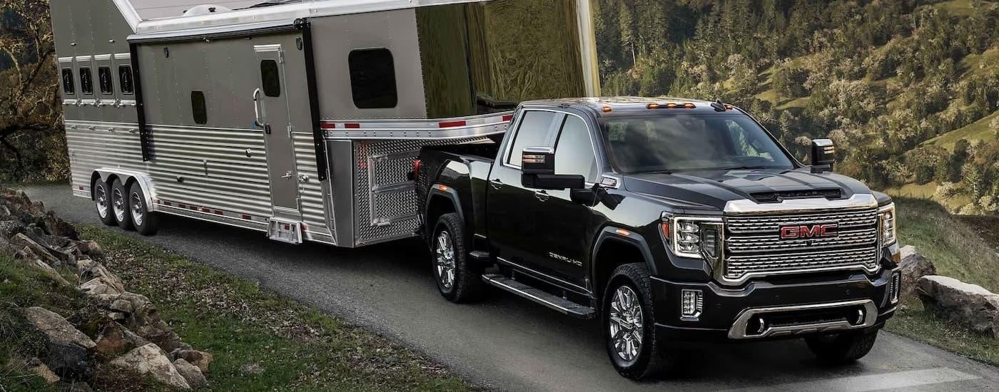 A black 2023 GMC Sierra 2500 HD Denali is shown towing a silver trailer on a mountain road.