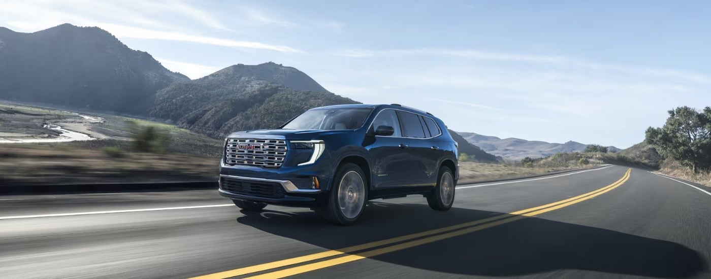 A blue 2024 GMC Acadia Denali driving on an open highway.