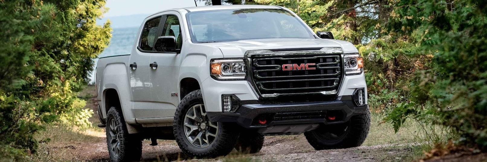 A white 2022 GMC Canyon is shown driving on a dirt road after leaving a used GMC dealer.